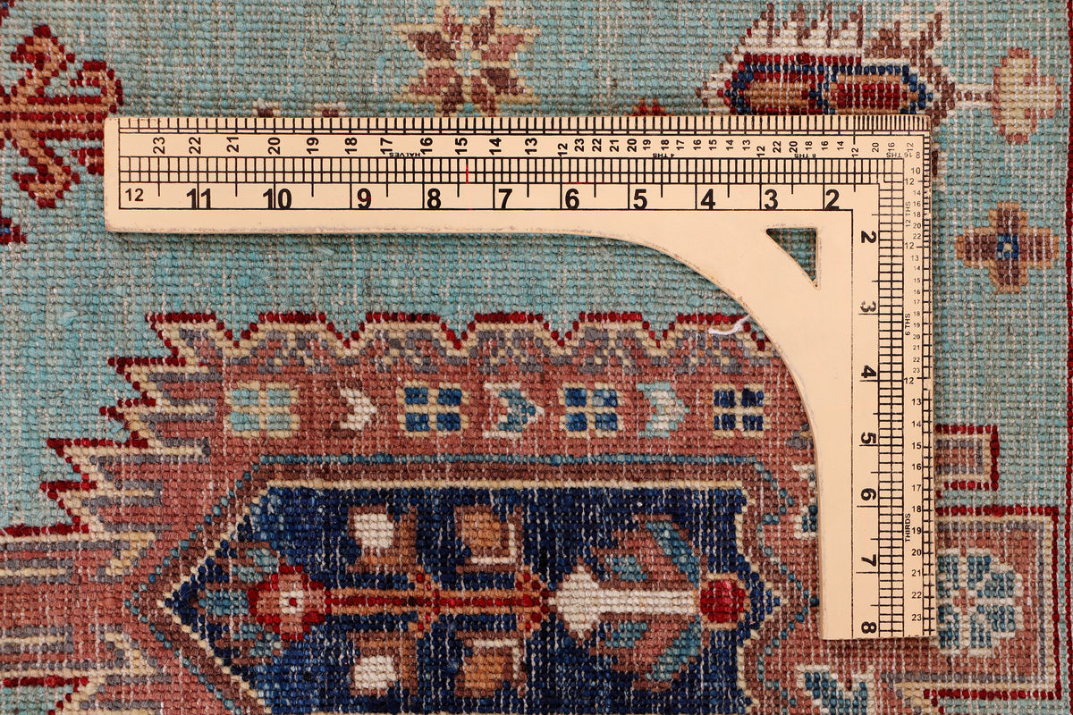 Turquoise rug with geometric motif border and ruler measuring the edge