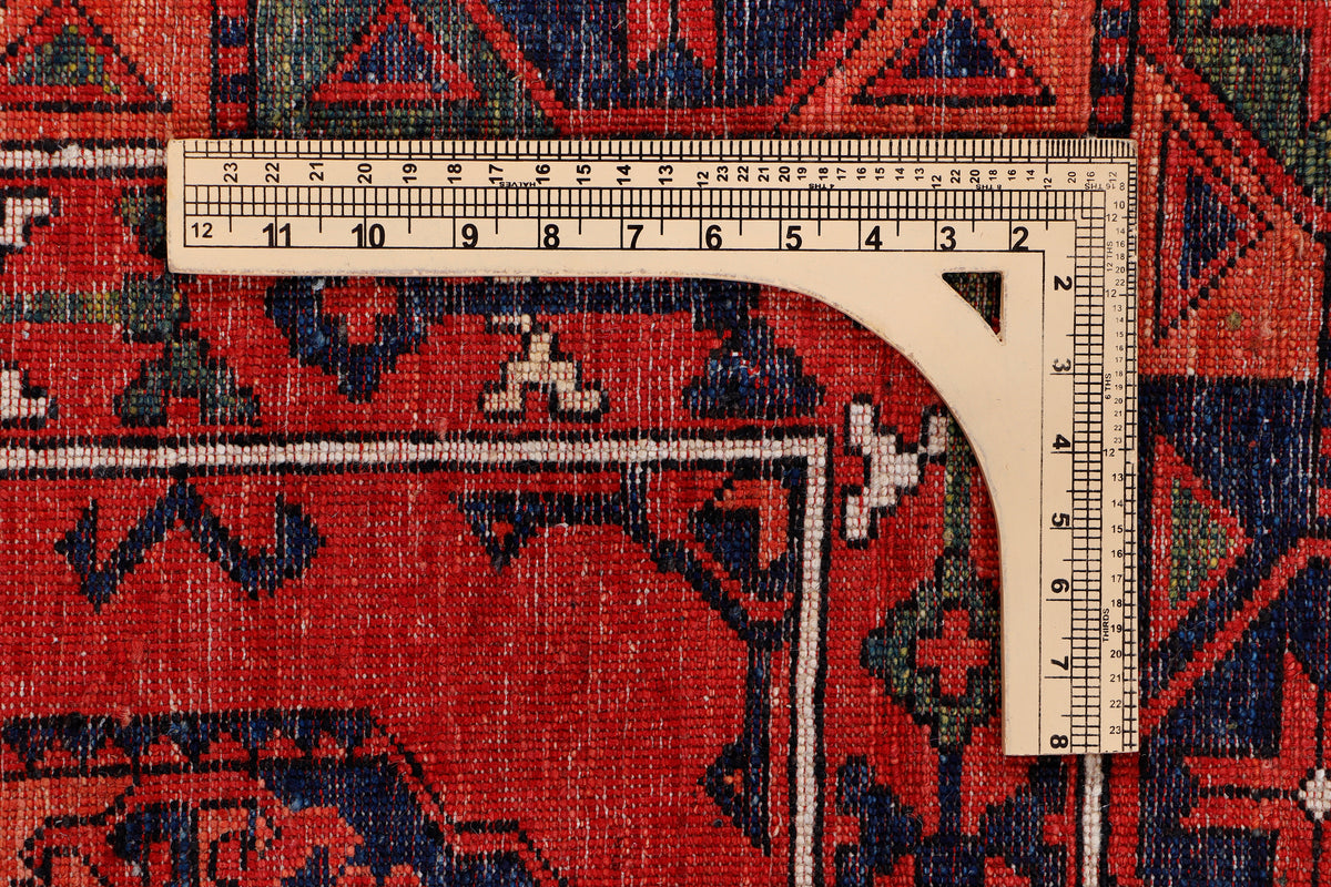 Red rug edge with multicolor geometric motifs and a measuring tape