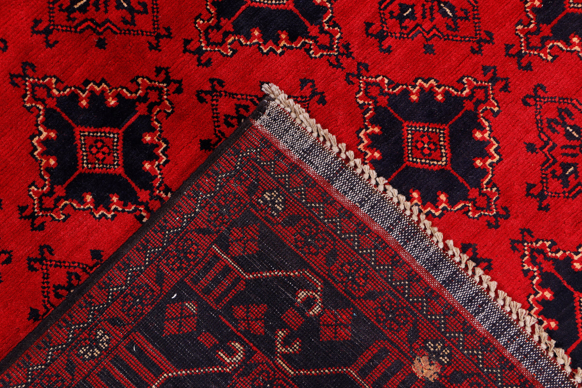 Red rug corner with diamond motifs and short fringe along the stitched edge