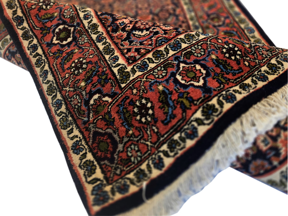 Bidjar rug corner detail with multicolor motifs, dark background, and beige edging fringe.