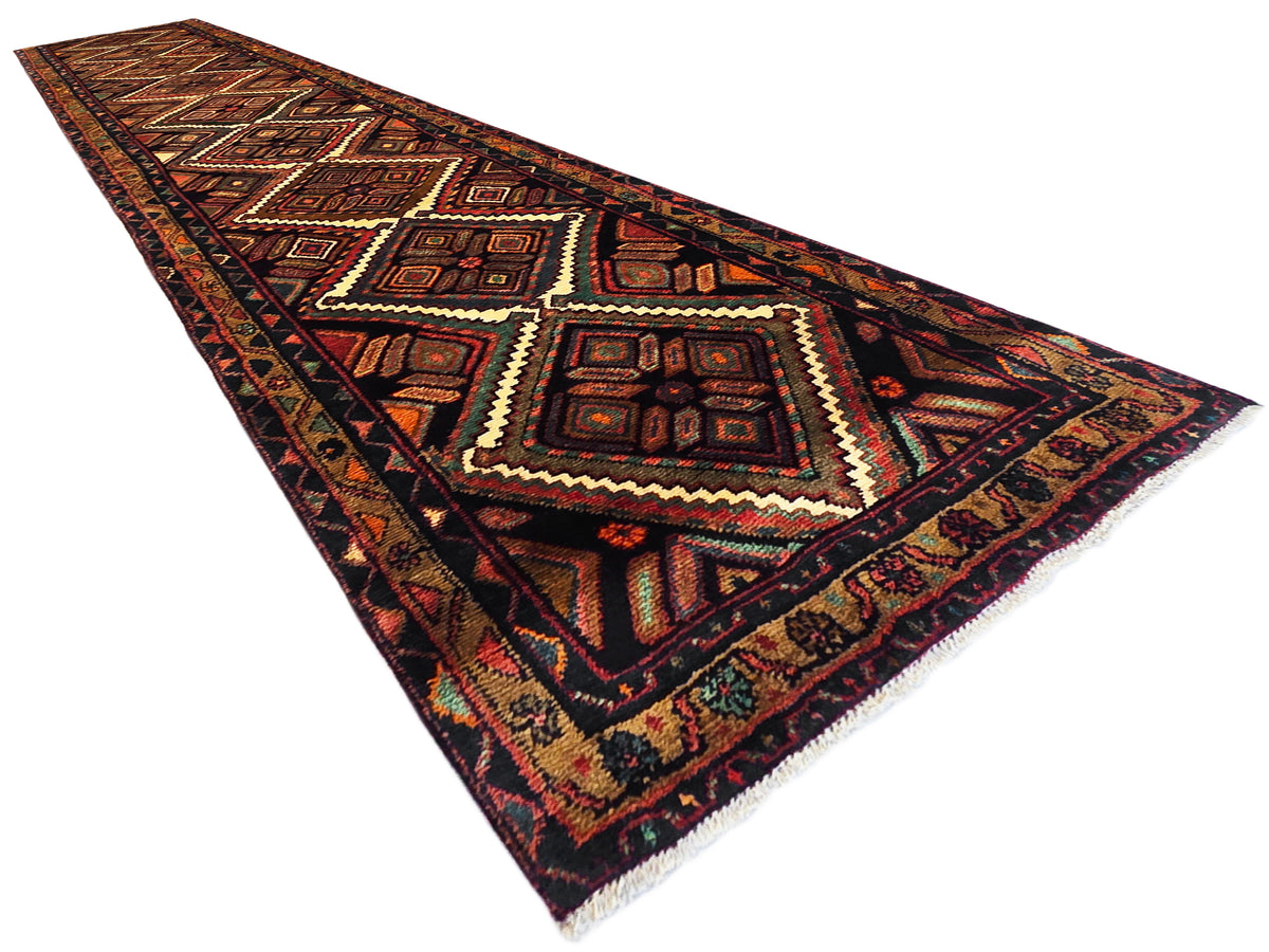 Hamedan rug runner angled view with repeating diamond motifs and zigzag border in dark tones