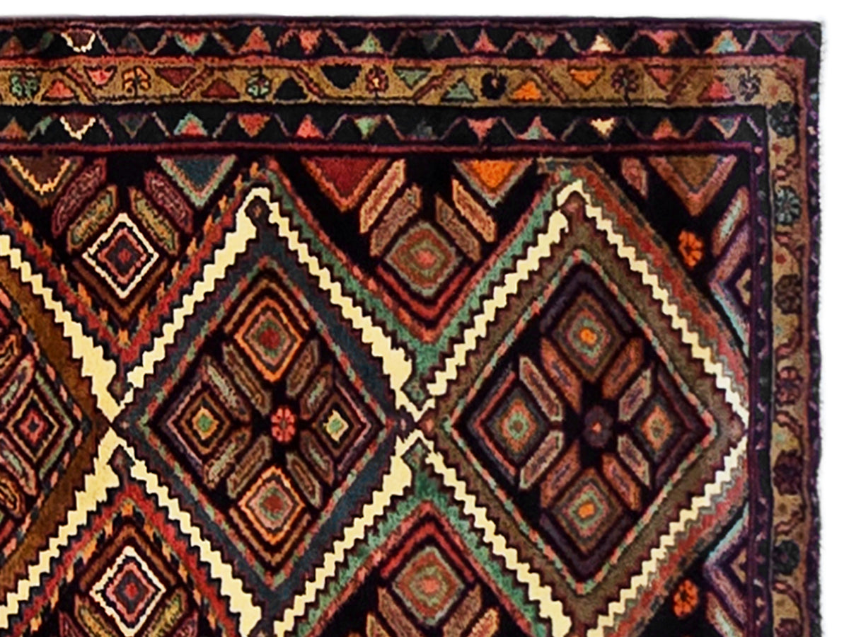 Hamedan rug close-up showing geometric diamonds and zigzag border in rust and navy