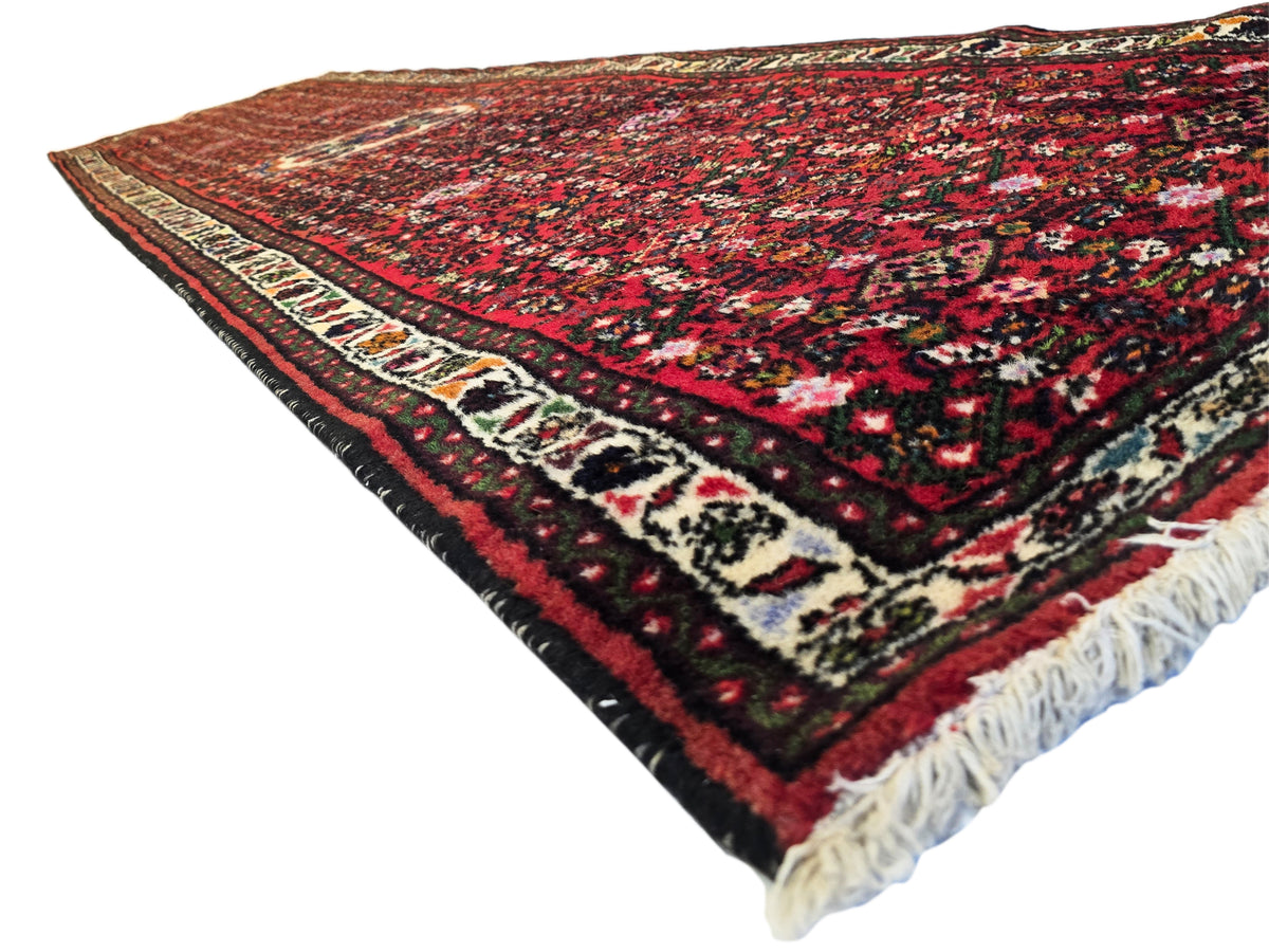 Red runner rug with geometric border, dark center field, cream accents, and white fringe
