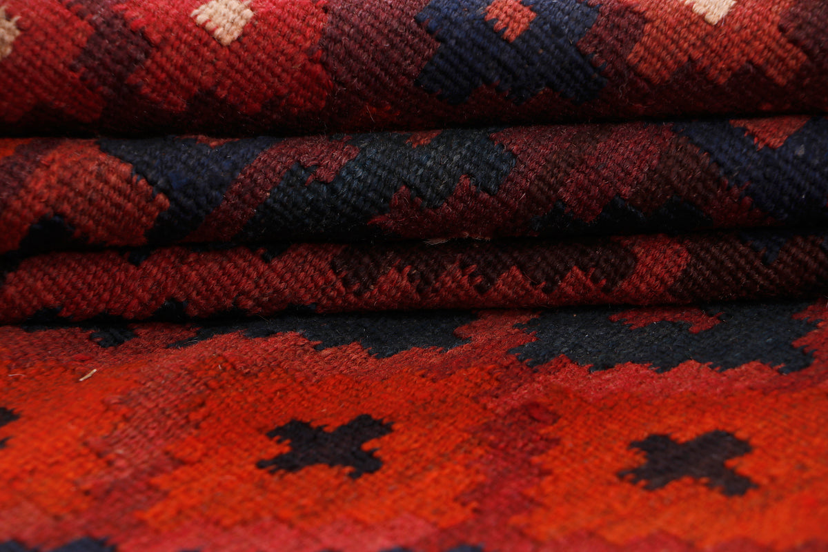Kilim rug close-up showing crimson red and navy bands with cream accents, textured weave