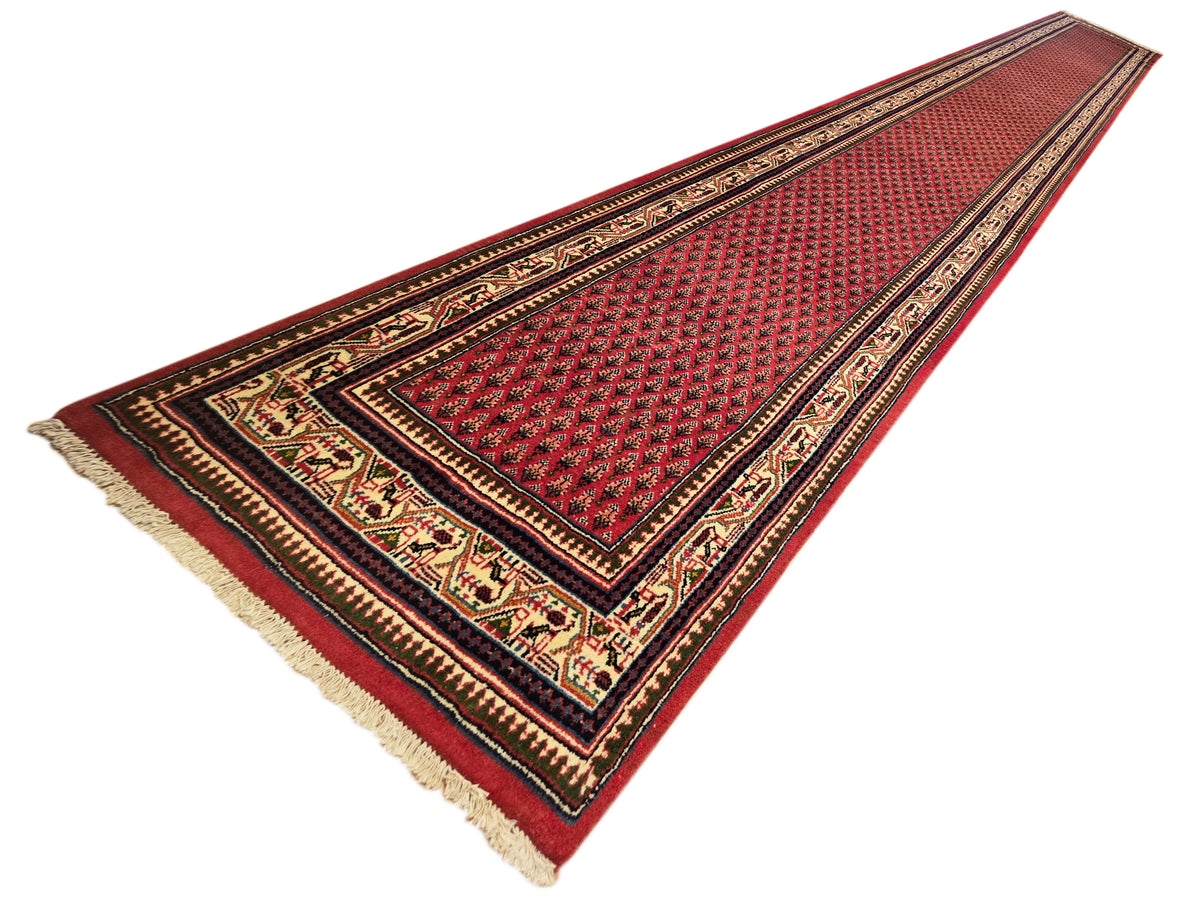 Red patterned runner rug with dark geometric border and light fringed ends