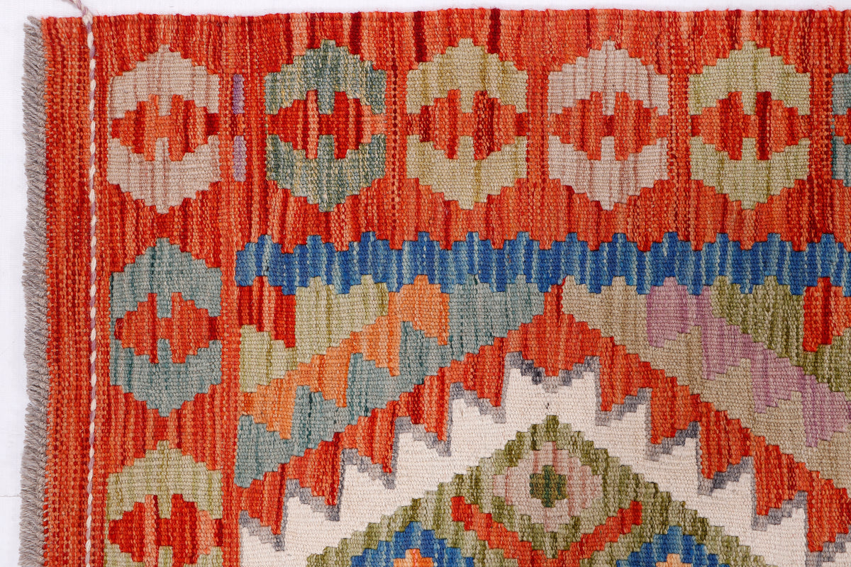 Kilim rug close-up with orange border and beige ground featuring blue and green diamond motifs