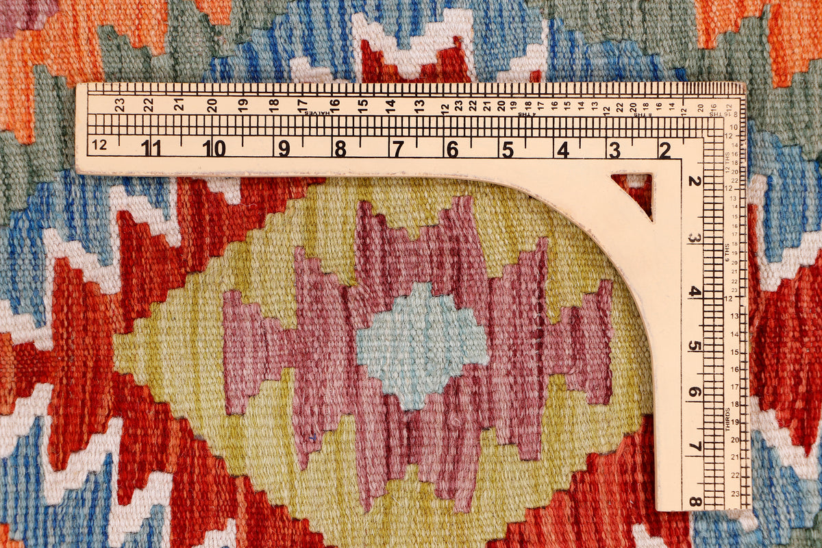 Geometric kilim rug close-up with ruler measuring woven red, blue, and cream sections