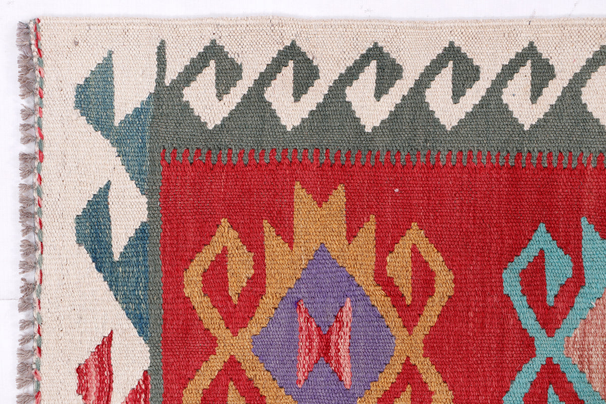 Kilim rug corner detail with cream base and red, gray, blue, and fringe trim