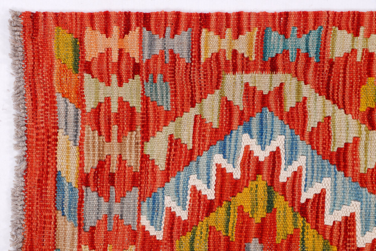 Kilim rug close-up showing red, light blue, cream, and green geometric motif.