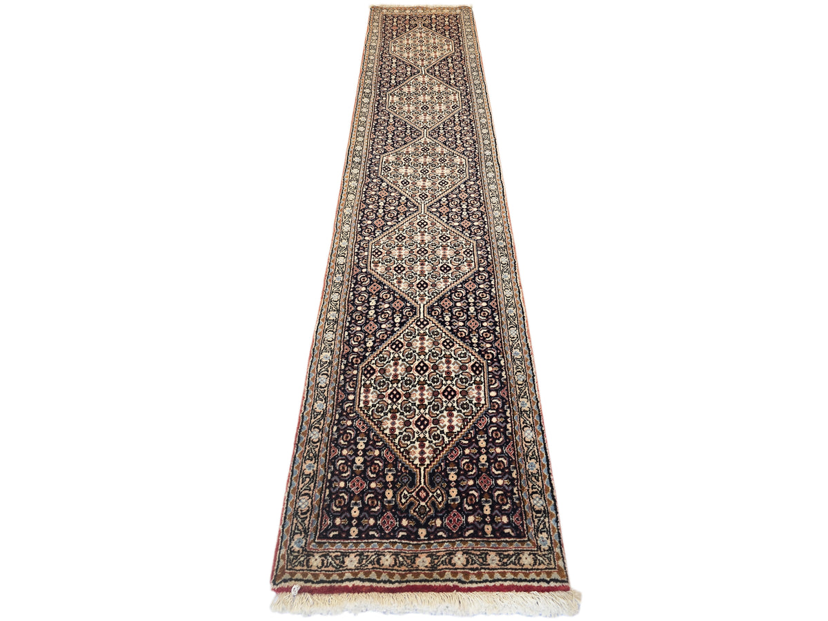Narrow geometric runner rug with central medallion, tan border, and short cream fringe