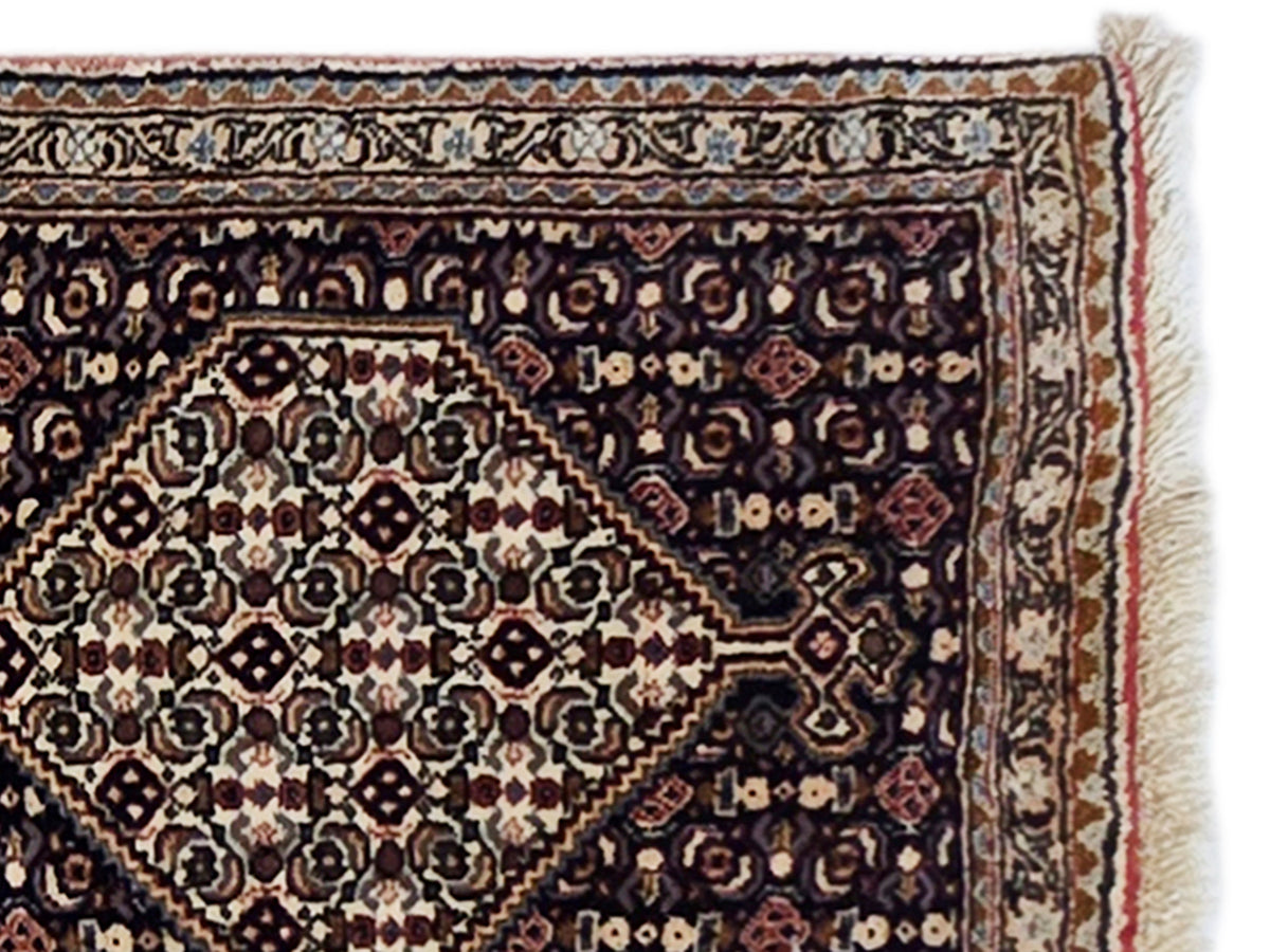 Close-up of dark patterned rug with central diamond motif and bordered trim fringe