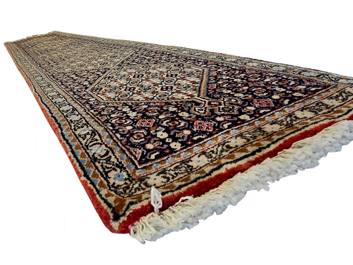 Rectangular patterned runner rug with central medallion, warm red border, and cream fringe