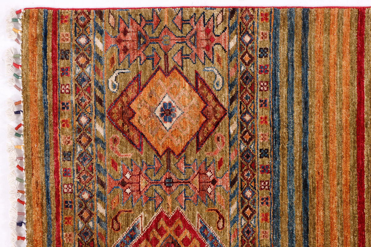 Green-toned geometric rug with central diamond medallion and colorful border fringe