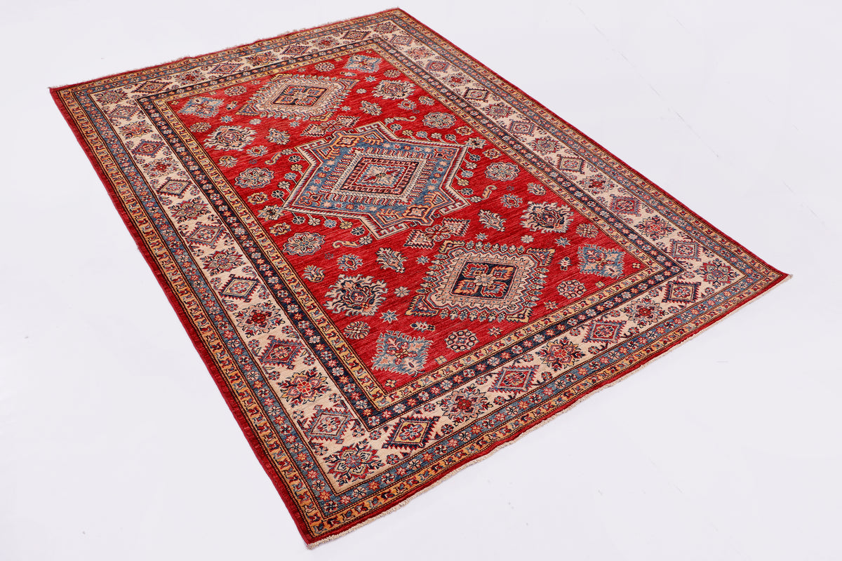 Kazak rug laid flat diagonally, red field with ornate blue and ivory designs