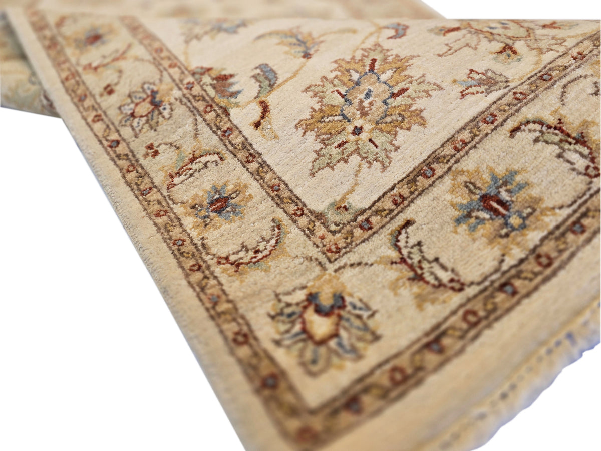 Close-up of beige floral runner rug corner with ornate border and fringe