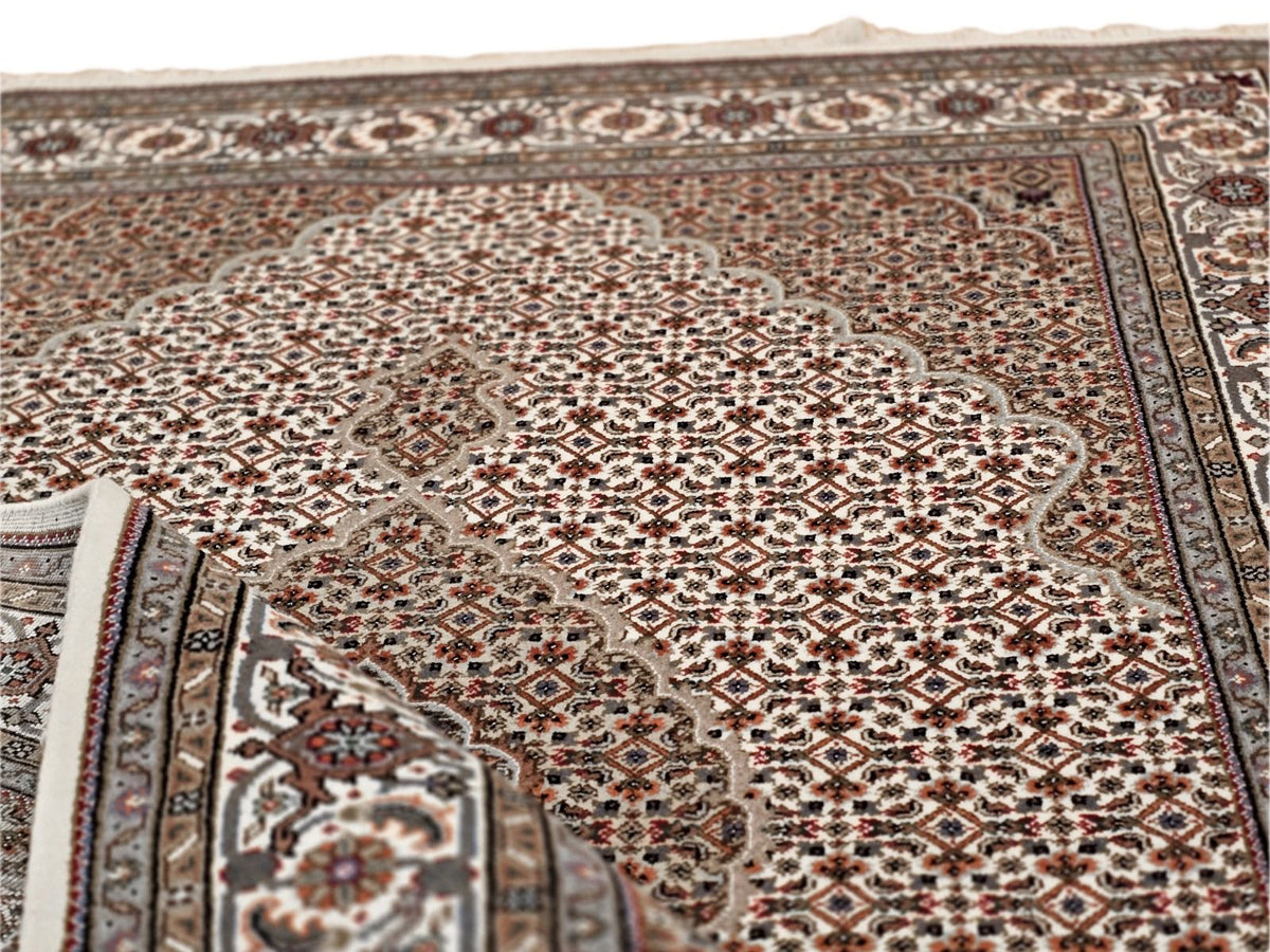 Corner of oriental rug with brown-and-cream diamond motifs and decorative border striping