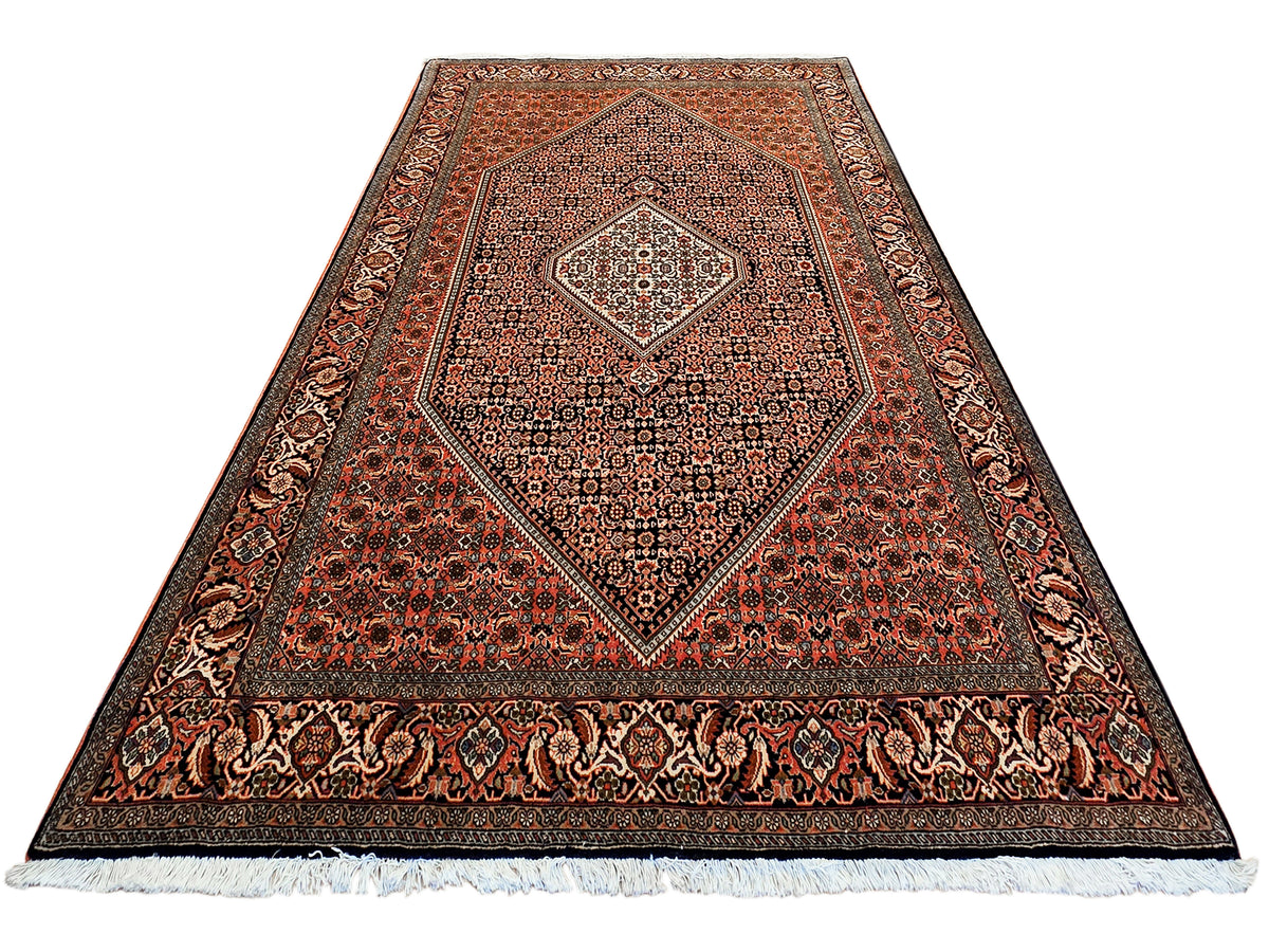 Rust and black ornate area rug with diamond medallion and cream accent details, fringe hem.