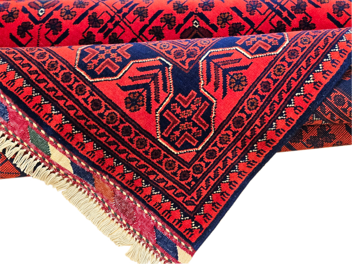 Red rug corner with navy lattice pattern and beige fringe trim