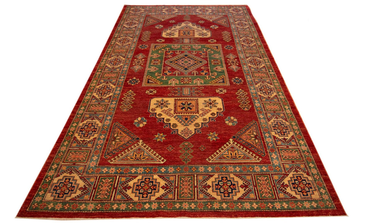 Rectangular red rug with ornate geometric border and central medallion, angled view