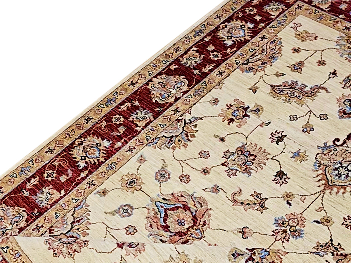 Diagonal view of cream rug with red band border and multicolor floral ornament accents.