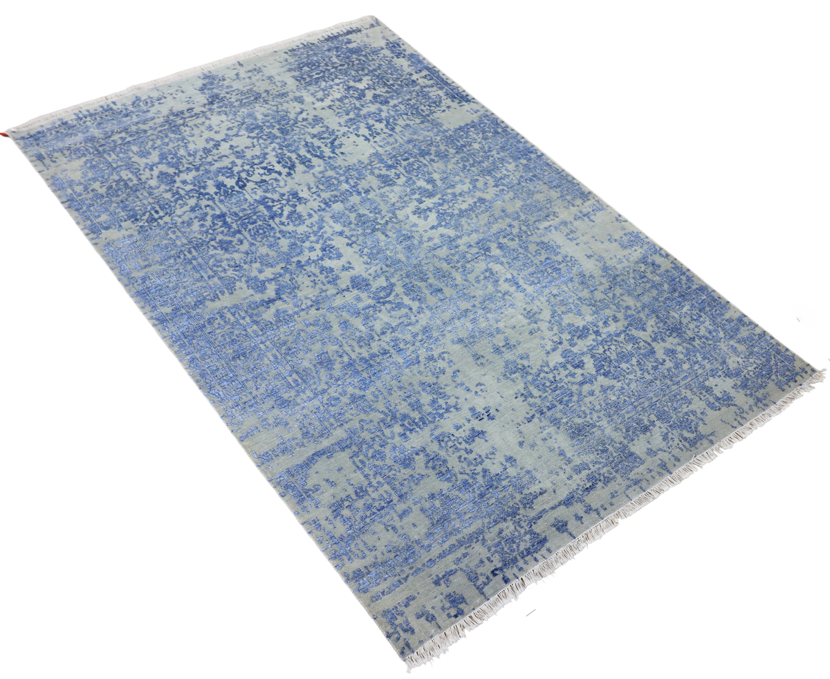 Blue mist rug with distressed allover pattern and short fringed edges, angled view.