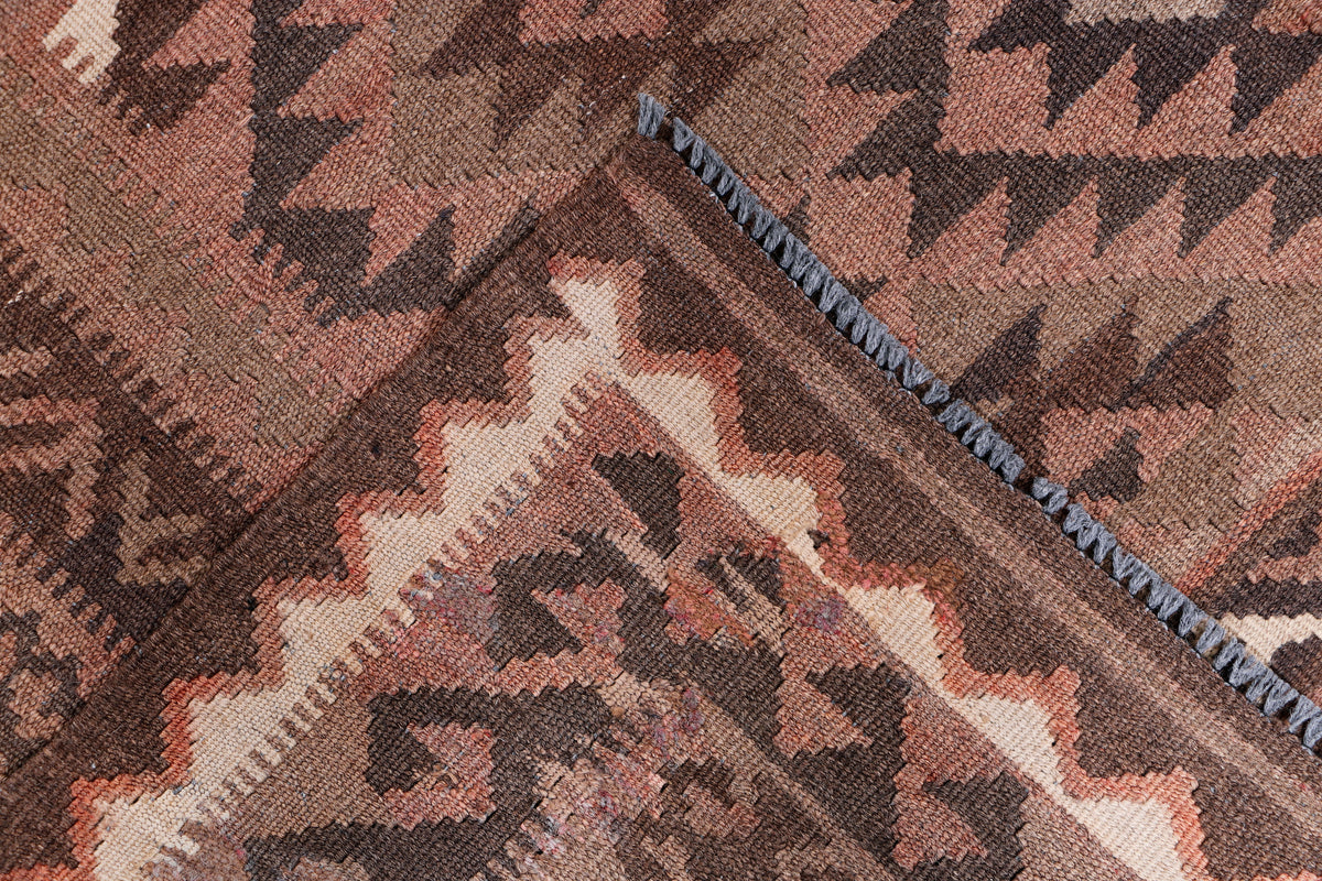 Brown kilim rug corner close-up with navy and rust geometric motifs and fringe