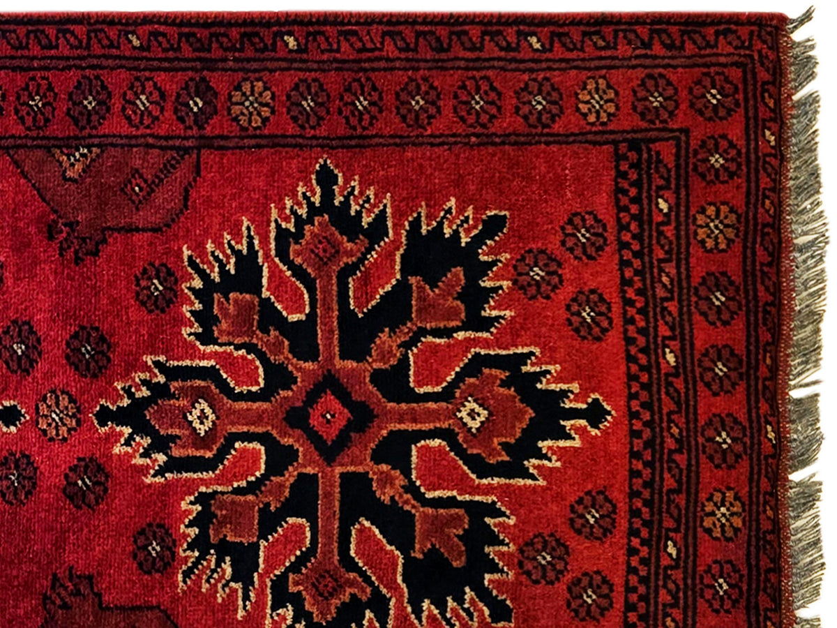Close-up of red Afghan rug with central starburst motif and dark ornamental border.