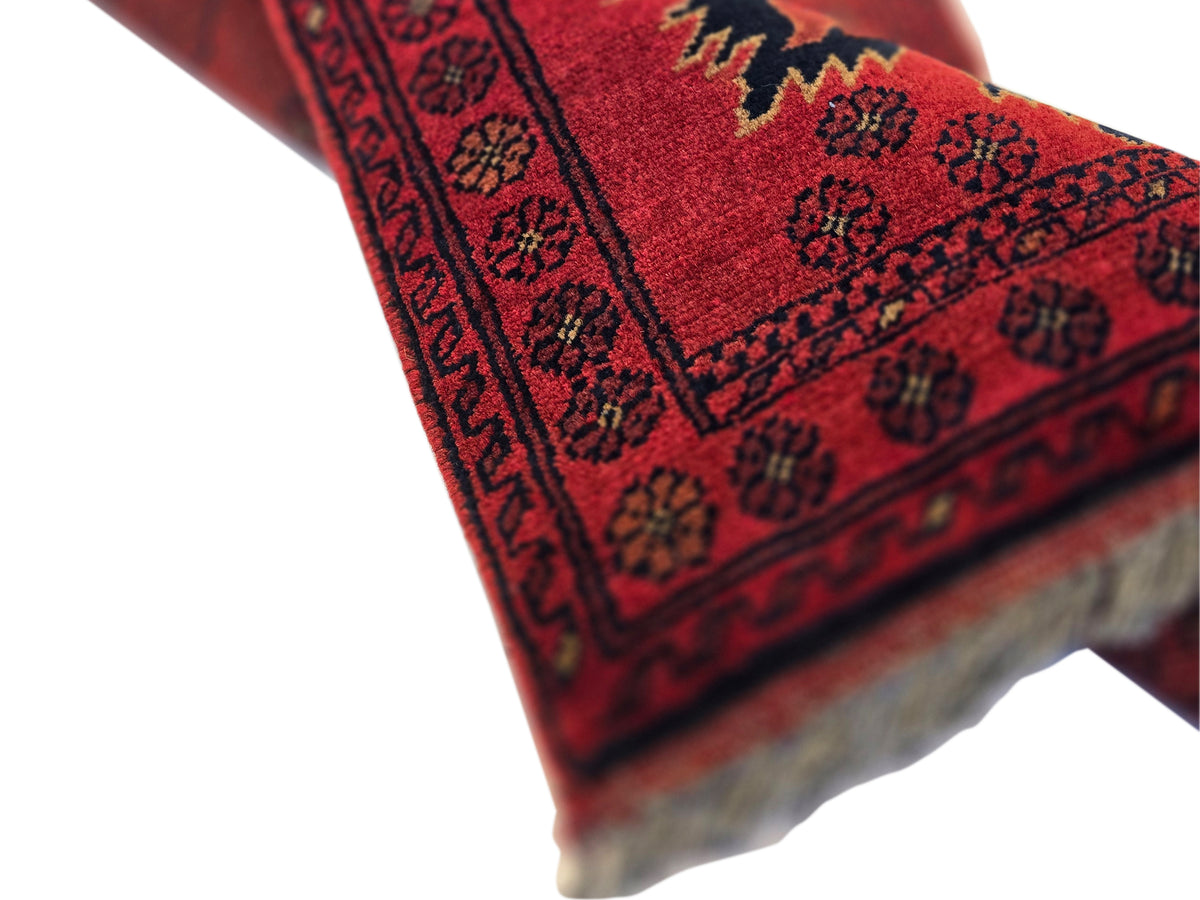 Red Afghan rug corner detail with patterned border and short fringe along the edge.