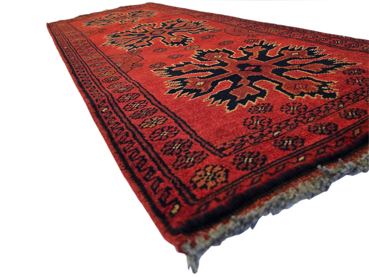 Red geometric Afghan rug with large center motif and patterned border, fringed edges.