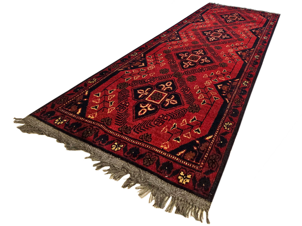 Red geometric Afghan-style runner rug with diamond motifs and short fringe border