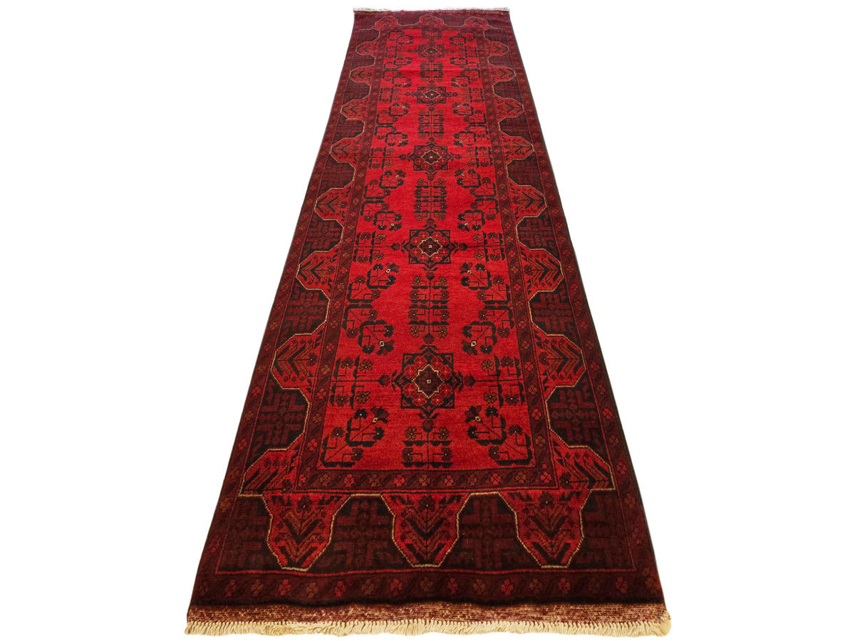 Red runner rug with dark geometric motifs and border, tan fringe at bottom edge