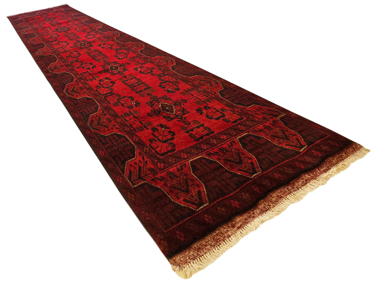 Red runner rug with dark medallion motifs, patterned border, tan fringe at corner ends