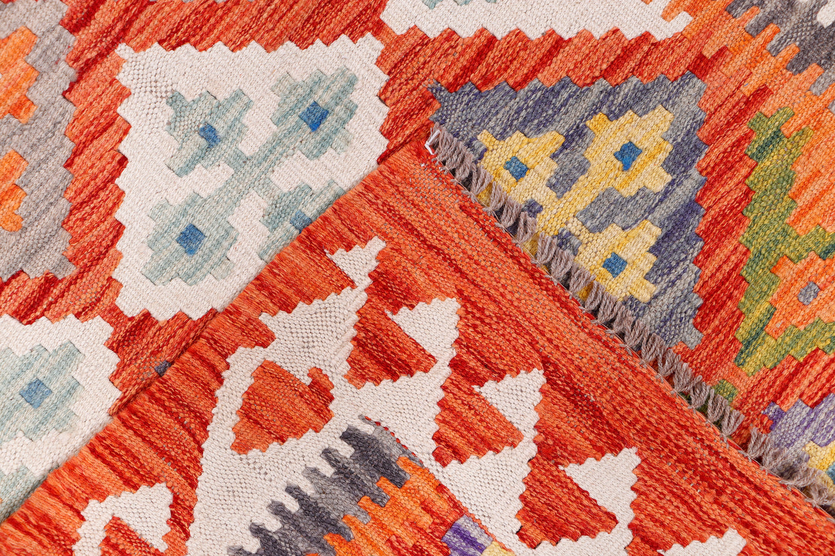 Orange kilim rug corner detail with geometric diamonds and stitched fringe edge