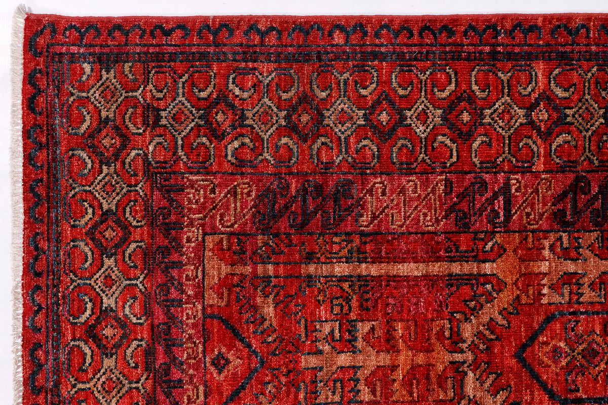 Red patterned rug with dark border and central geometric panel, close-up