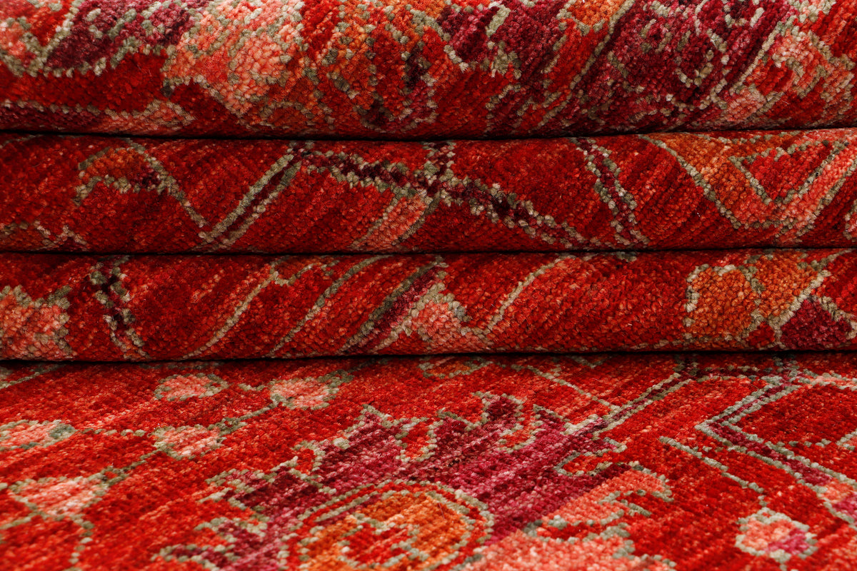 Folded red patterned vintage area rug with intricate motifs and border design.