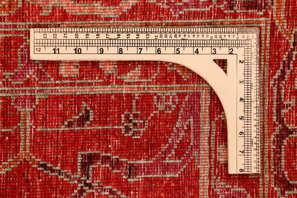 Red vintage rug edge with white measuring tape along the border for size.