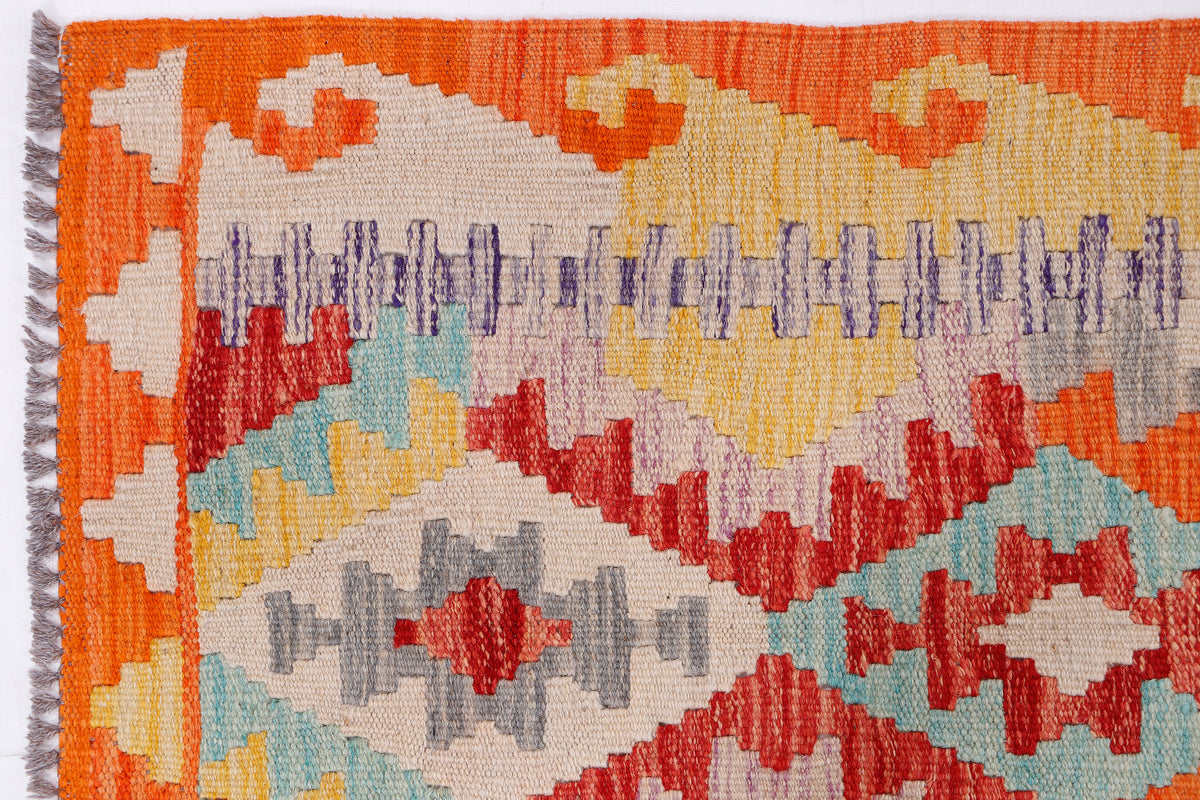 Kilim rug close-up with orange border and multi-color geometric motifs, woven texture