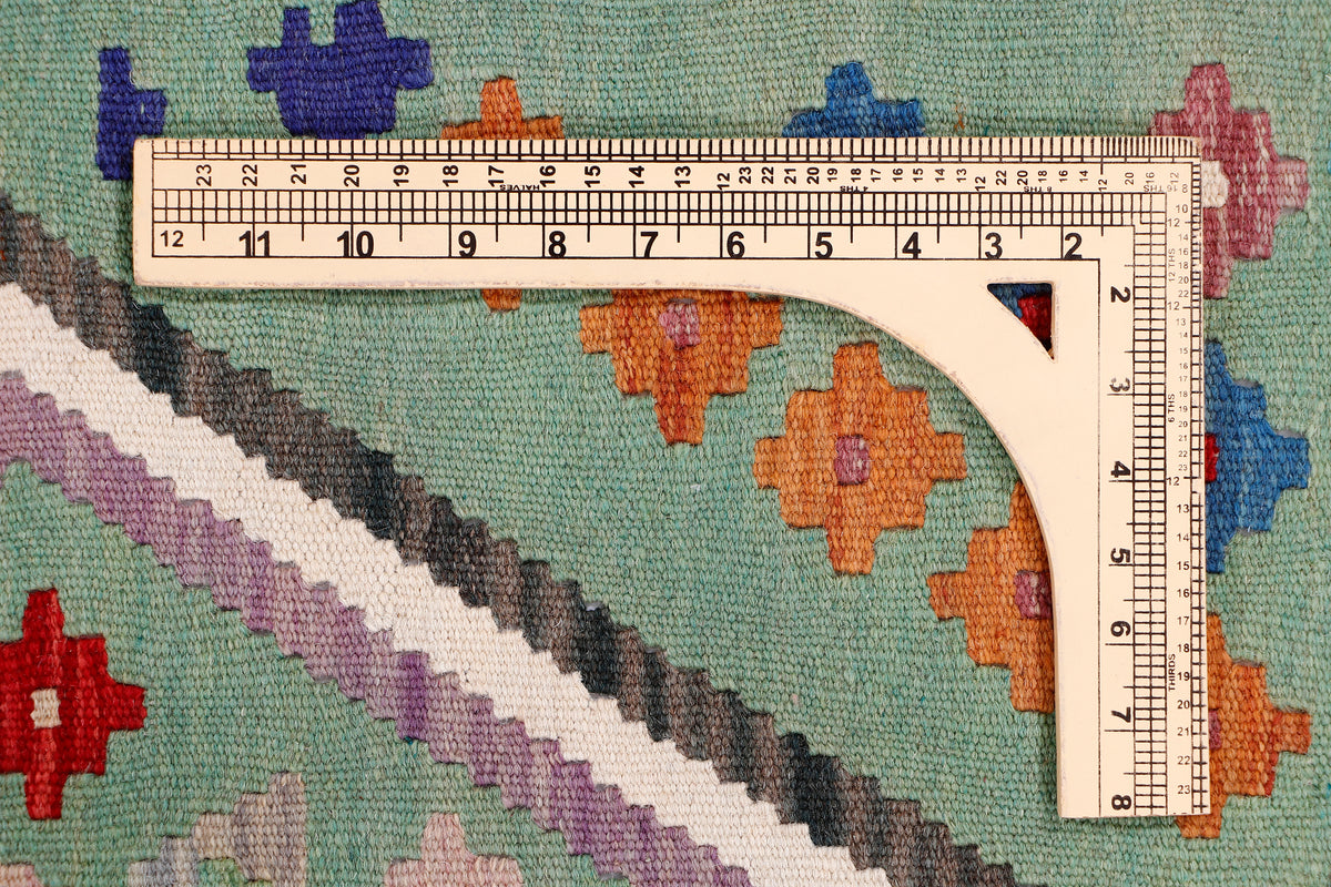 Green kilim rug corner with measuring tape, multicolor geometric pattern along edge