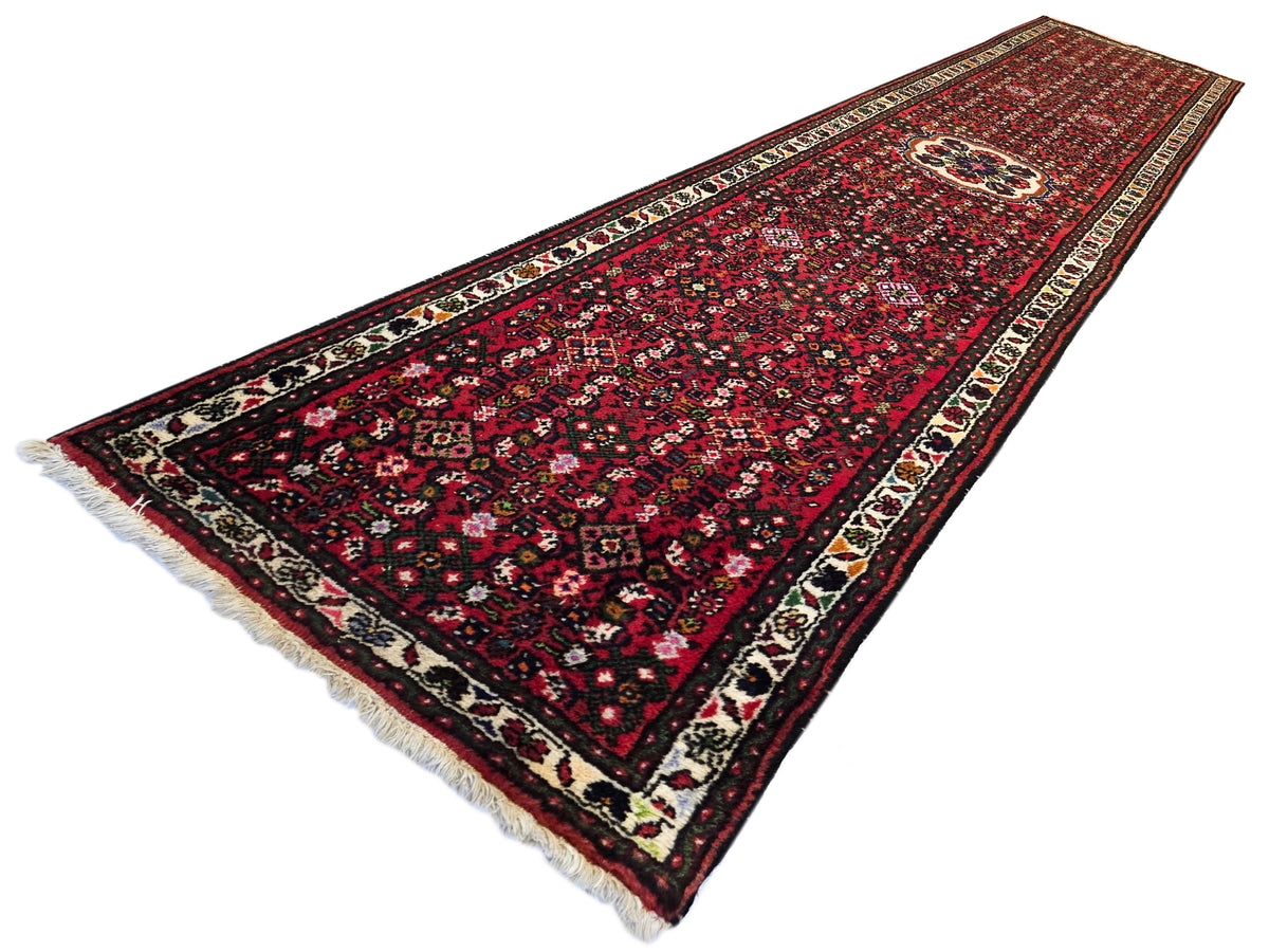 Runner rug with angled view, red and burgundy floral pattern, cream border, fringed edge