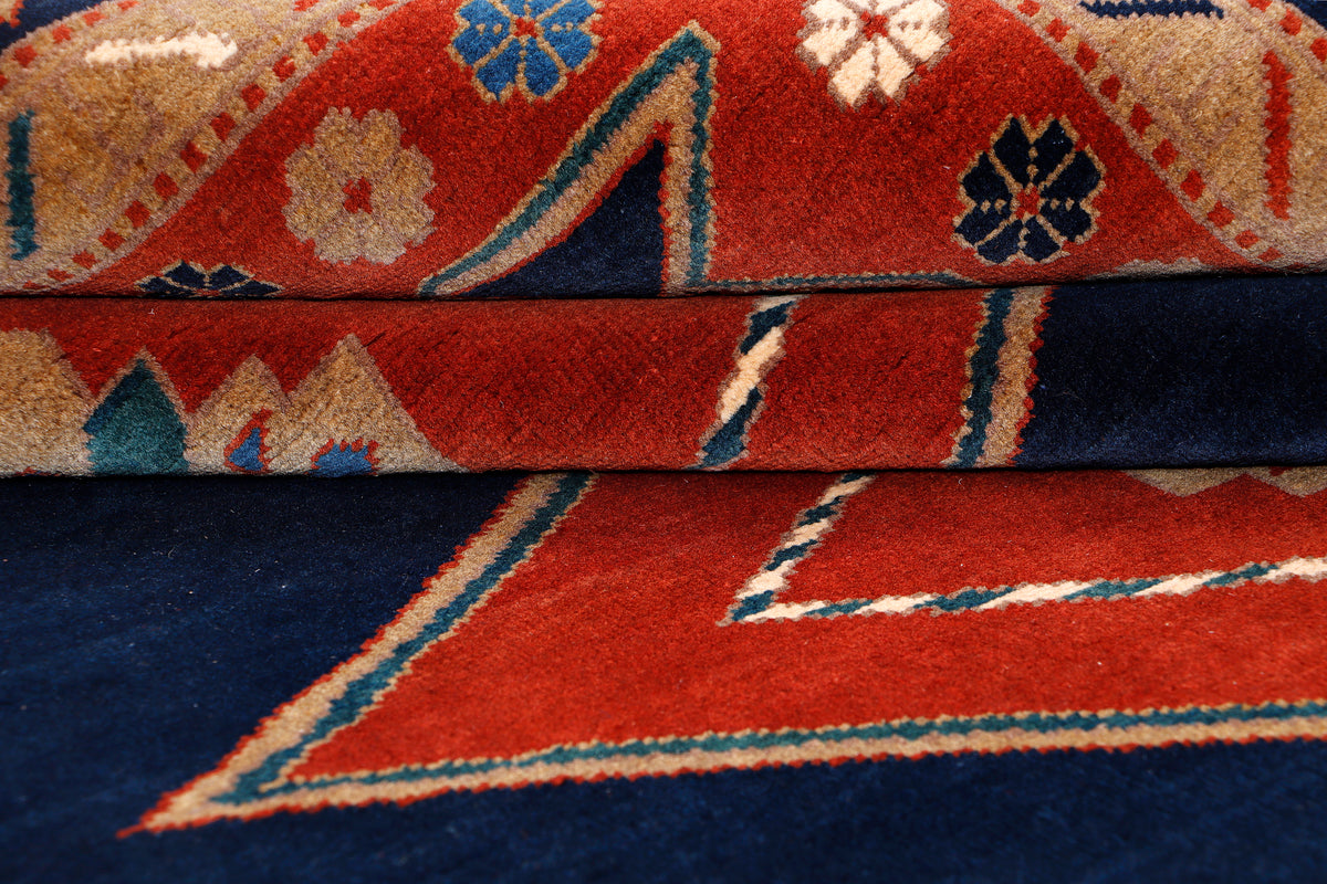 Close-up of rug pattern showing blue ground with red and teal geometric shapes.