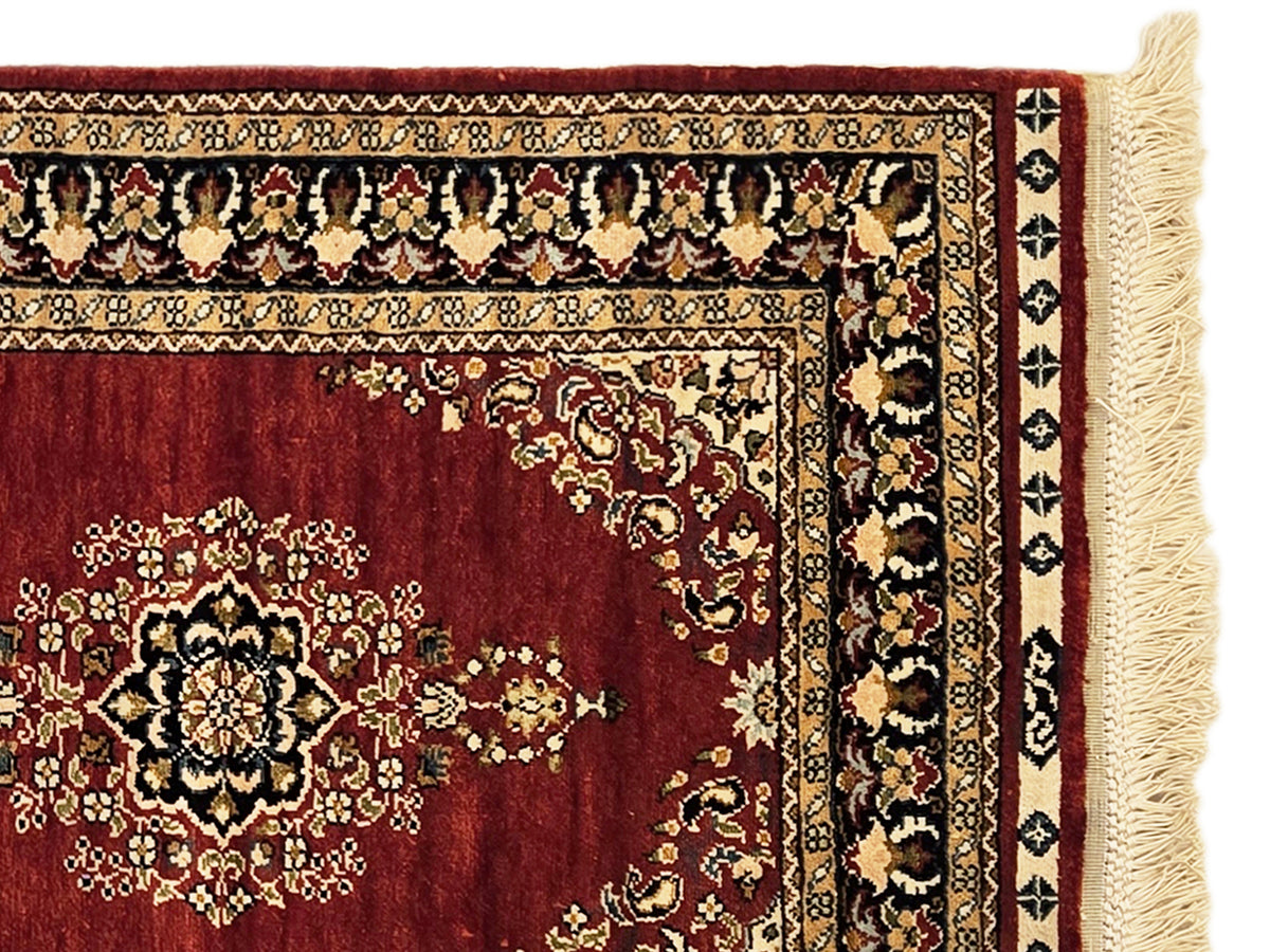 Hereke rug corner detail with deep red floral pattern, decorative border, and fringe