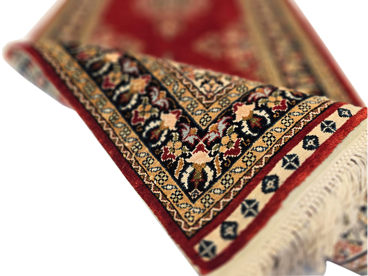 Hereke rug corner close-up with deep red background, ornate motifs, and beige fringe