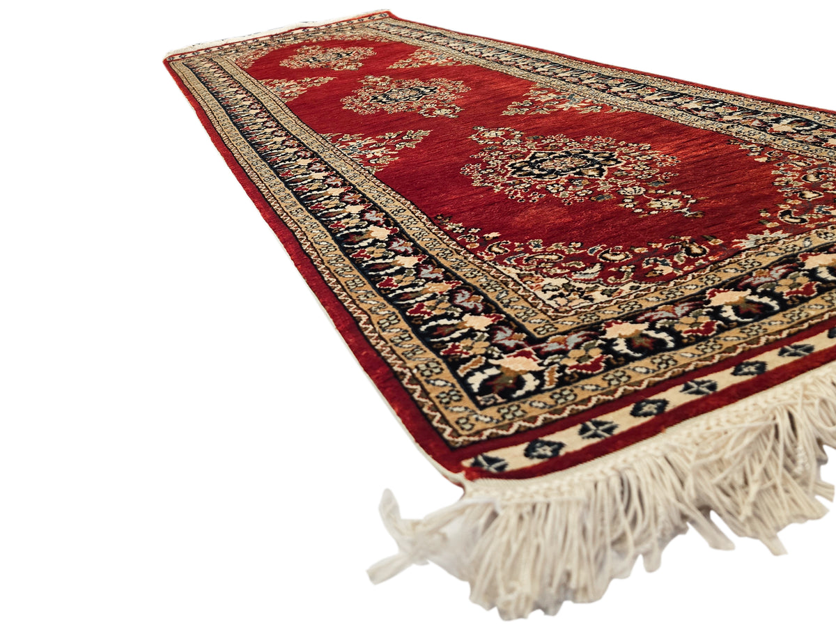 Hereke rug angled view in deep red with patterned border and cream fringe tassels