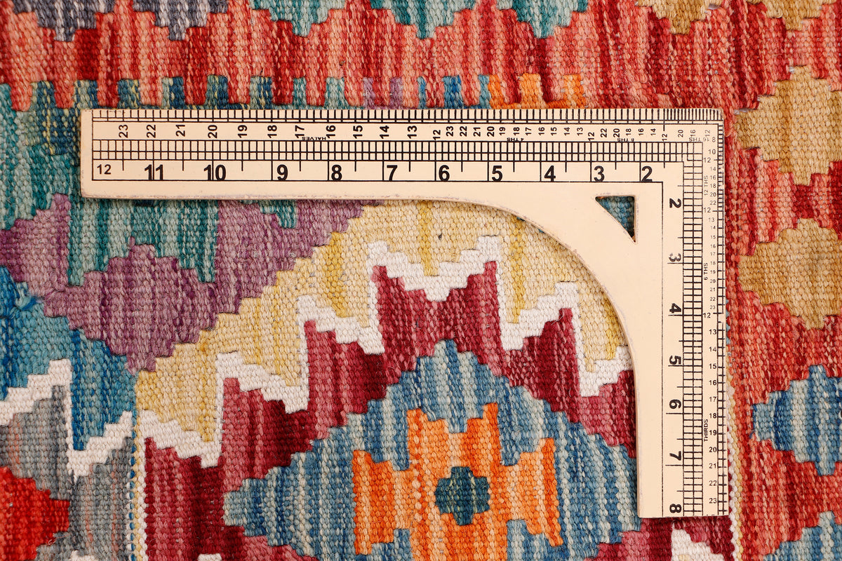 Kilim rug texture with ruler measuring over red, teal, and beige geometric pattern