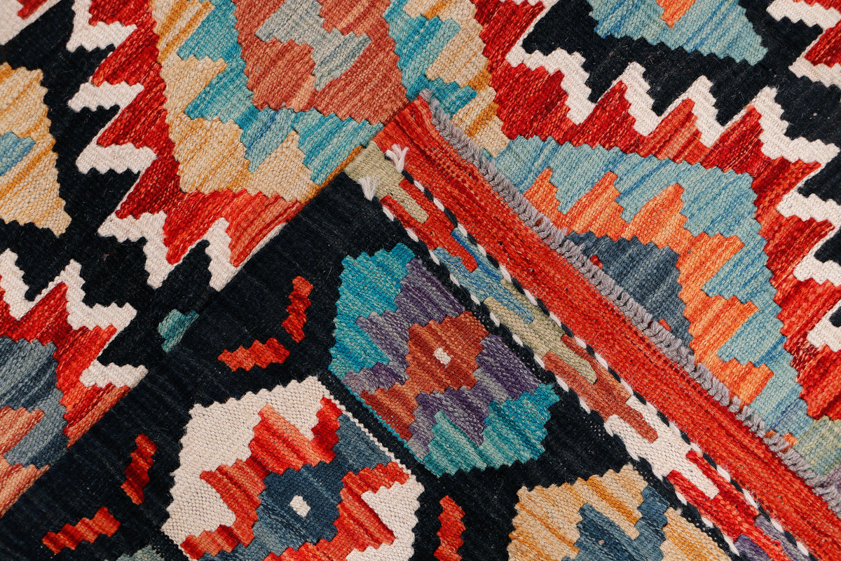 Kilim rug close-up with textured geometric blocks in black, red, teal, orange, and cream