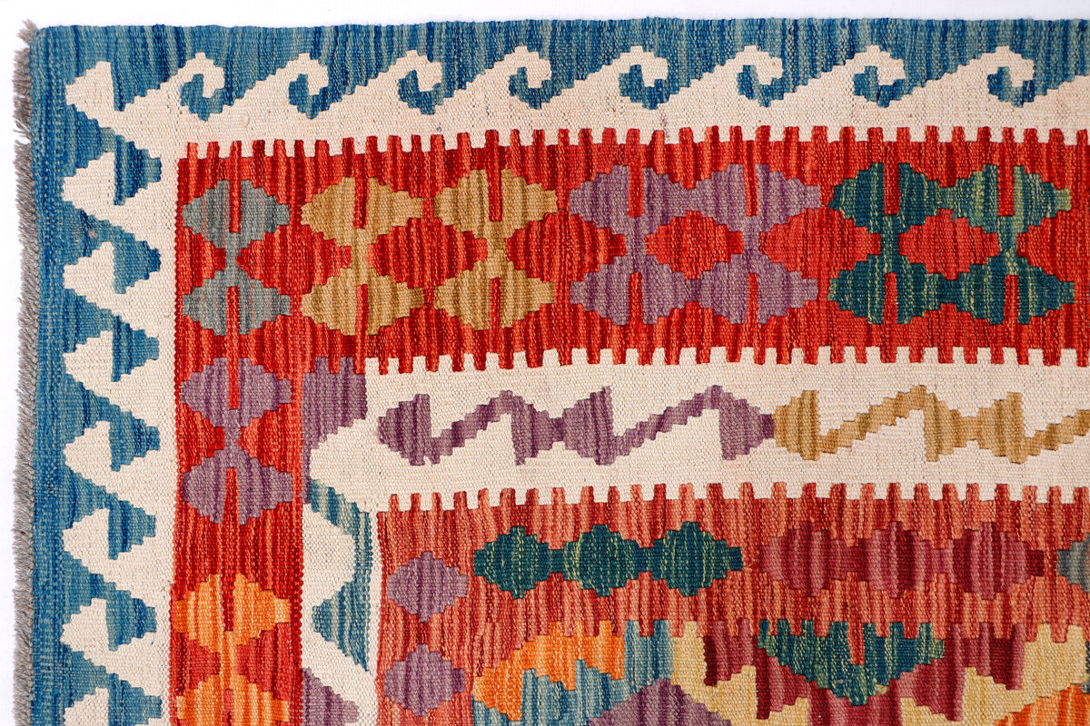 Kelim rug close-up with blue border, cream base, and red-green geometric motifs