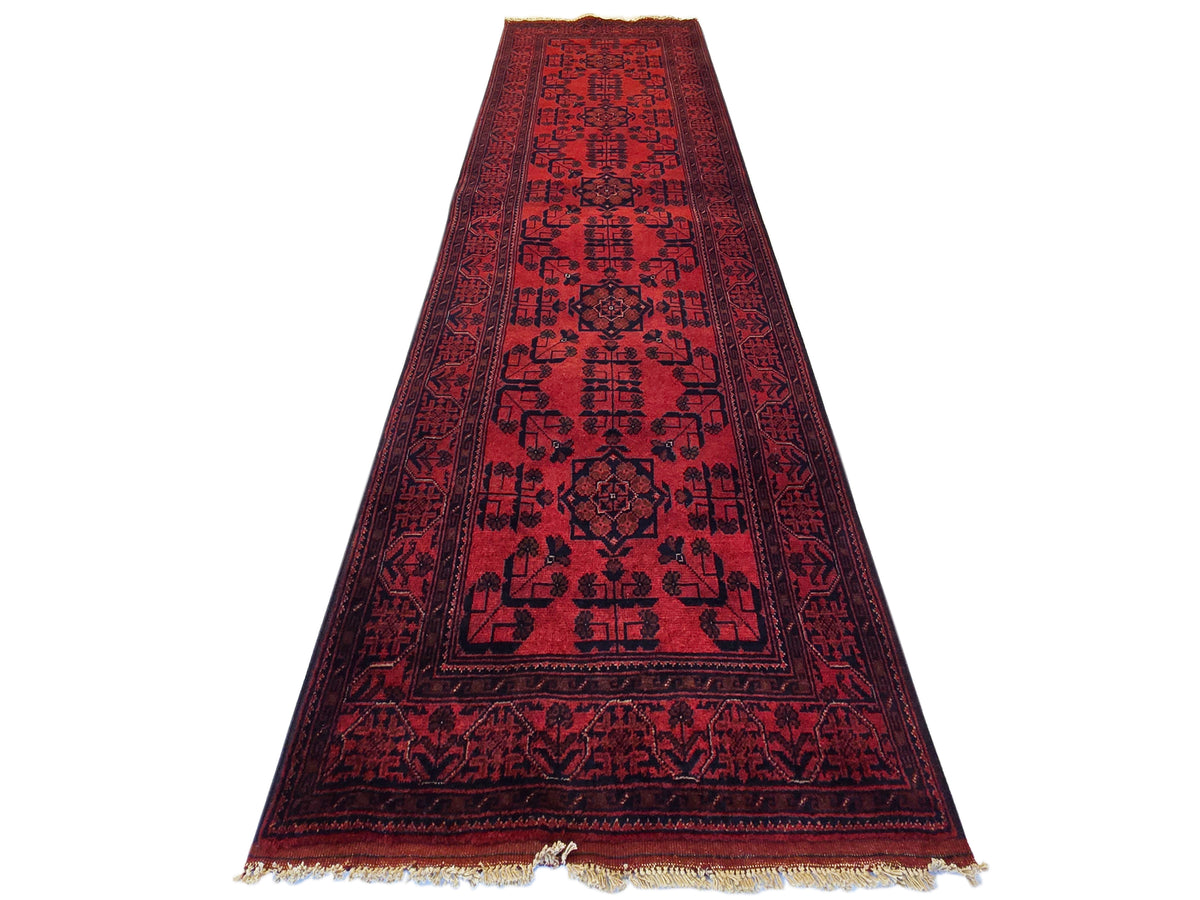 Khanmohamad rug runner in deep red with central medallion-like motif and fringed borders.