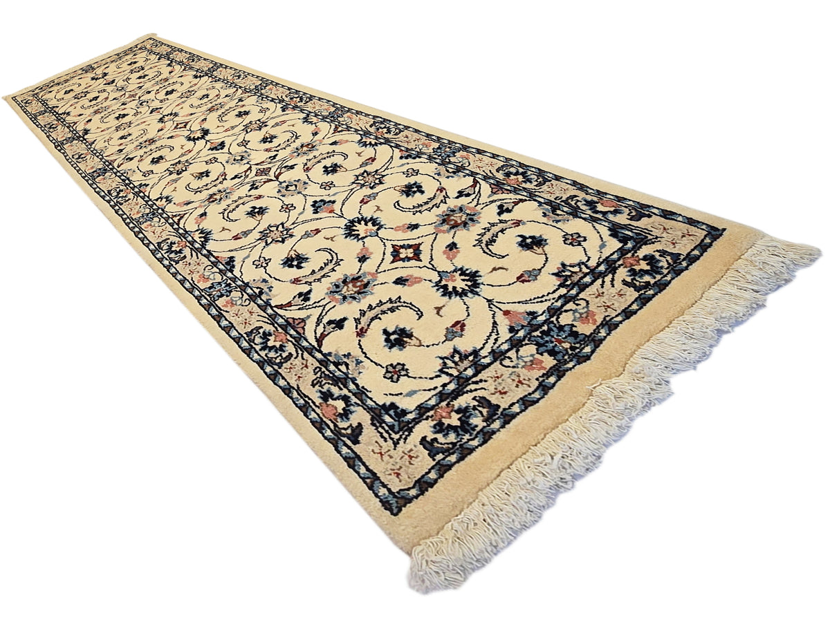 Rectangular runner rug with beige background, navy border, floral scroll motif, light fringe ends.