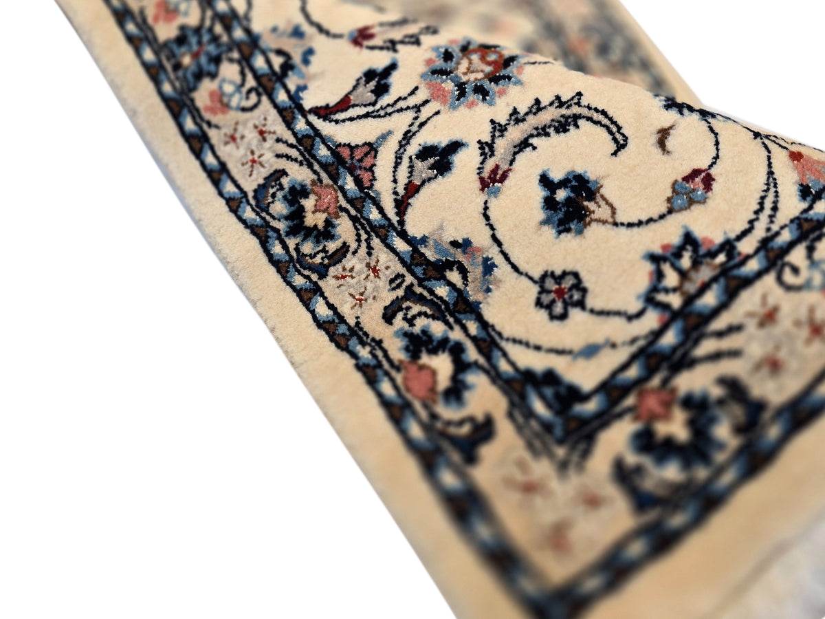 Corner detail of beige rug with navy lines and small floral accents, short fringe along edge.