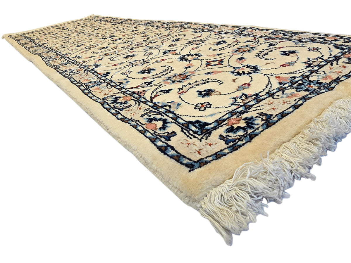 Runner rug with cream-beige center, dark blue floral border, and long fringed corners.